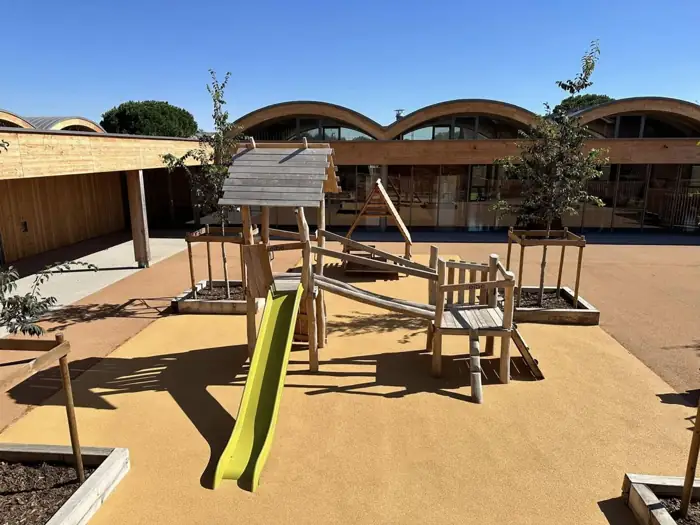 Cour de crèche avec sol souple ocre sous un jeu en bois